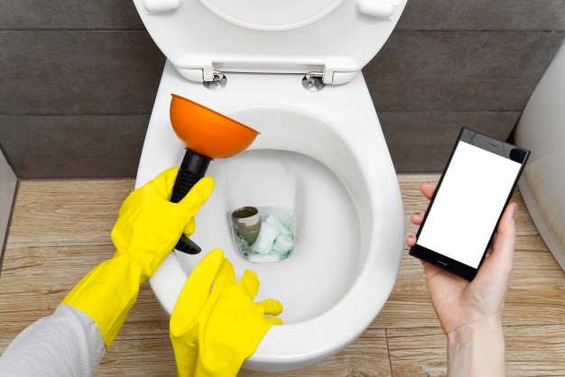 Clogged toilet, a person using a plunger, another person trying to contact a plumbing service