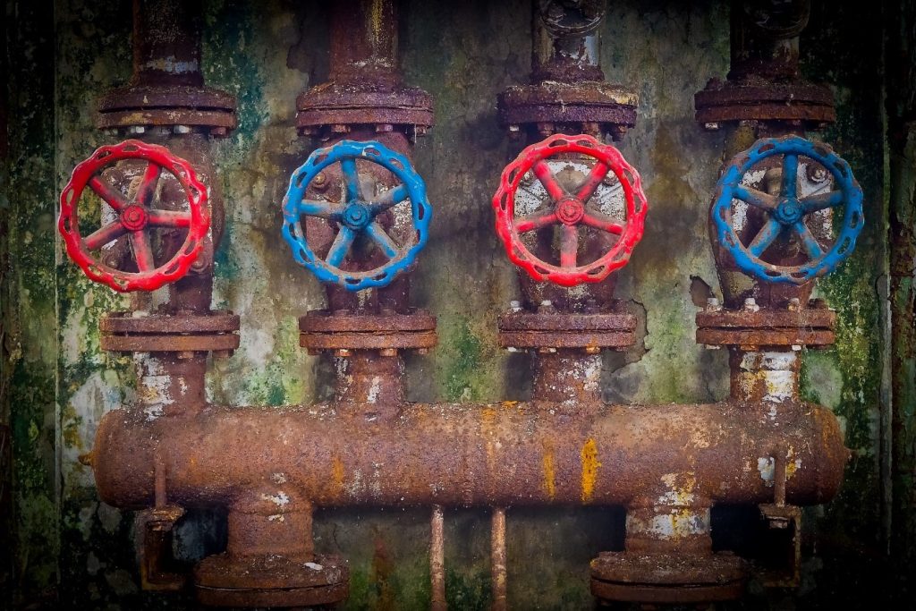 A set of four ill-maintained and rusted pipes with two red and two blue valves