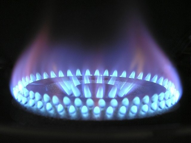 A burner below a traditional water heater with a blue flame.