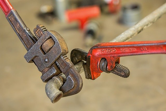 Plumbers using a pipe wrench to repair a rusty pipe.