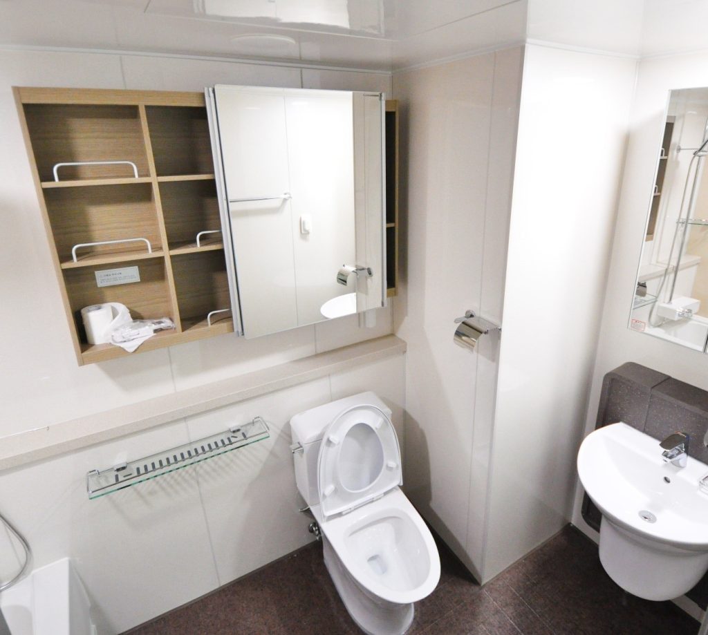 A bathroom with a toilet, faucet, cabinet, and mirrors