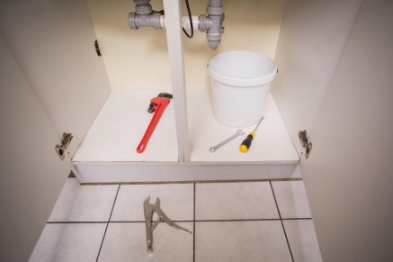 Plumbing tools and a white bucket under the kitchen sink.