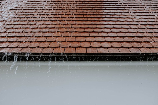 A brown roof with rainwater falling from its shingles