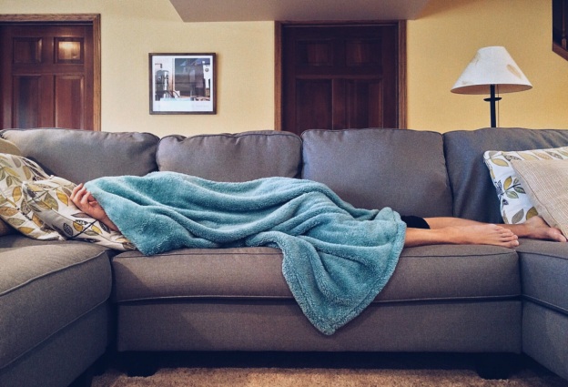 A person lying on the sofa while covered with a blanket