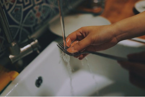 a person cleaning a fork on the kitchen sink
